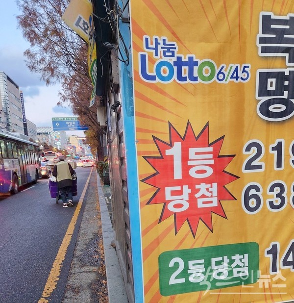 70대 노인이 폐지 손수레를 끌고 성남시 수정로를 걸어가고 있다. 로또 복권을 파는 인도 가판대가 설치한 복(권)명(당)이 보인다. [사진=정수남]