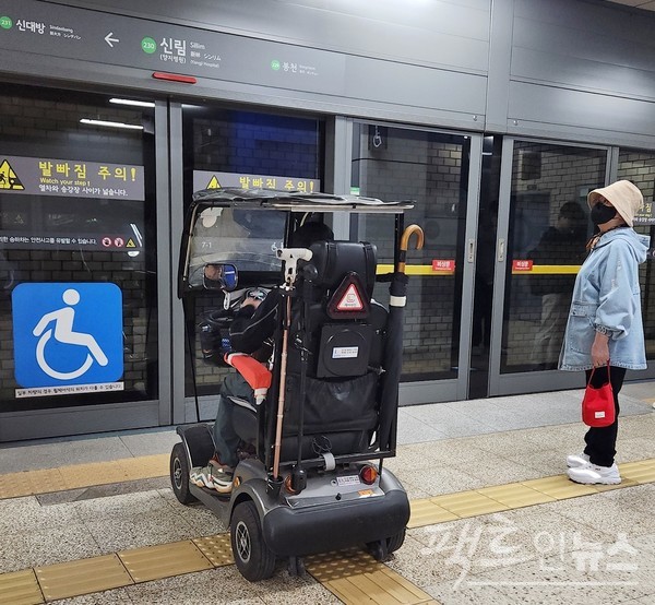 한 노인이 전동키트를 타고 지하철을 기다리고 있다. 각종 장치를 부착해 여느 전동차보다 크다. 승객이 멀찍이 떨여져 있다. [사진=정수남 기자]