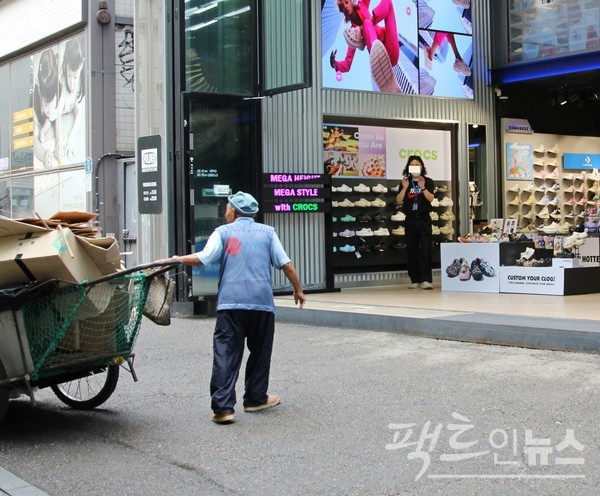 (위부터)한 70대 노인이 부동산사무실에서 가져온 페지를 손수레에 싣고 있다. 바료 옆에 있는 벤치에서 한 20대 여성이 스마트폰을 보고 있다. 노인이 바로 옆 신발가게로 가자, 이곳 종업원이 폐지가 없다는 수신호를 보내고 있다. [사진=정수남 기자]