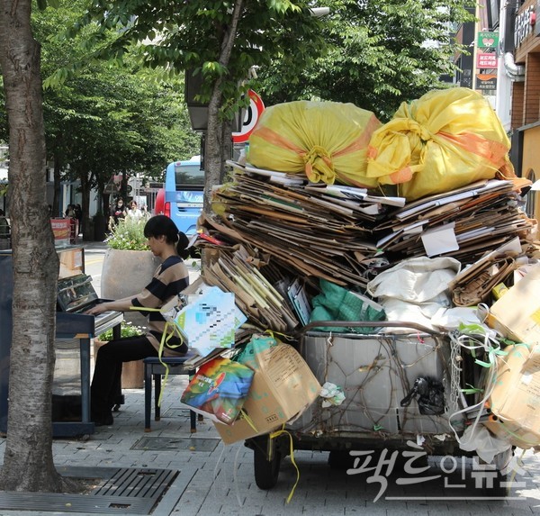 20대 남성이 연세로에 있는 피아노를 연주하고 있다. 바로 옆에는 폐지가 가득한 수레가 있다. 현재 국내 생계형 폐지 수집 노인은 1만5000명 정도다. [사진=정수남 기자] 