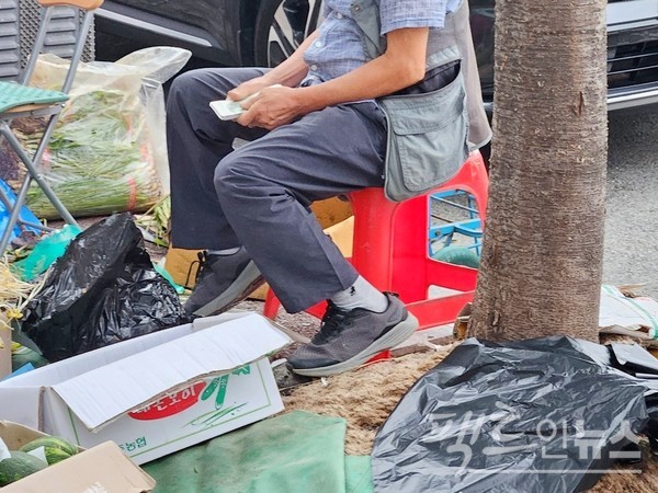 수도권 한 도시에 자리한 노점상. 상인이 채소 등을 한나절 판 돈을 세고 있다. [사진=정수남 기자]