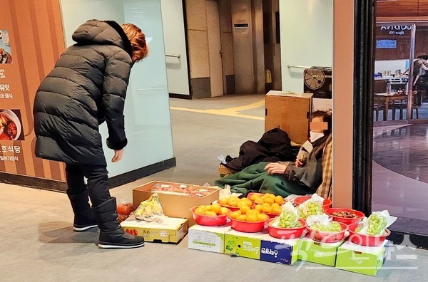 서울지하철 2호선 삼성역에 자리한 과일 노점 노인이 추위를 피하기 위해 이불로 몸을 싸맸다. 추위 때문에 손님이 와도 무덤덤하다. 퇴근 시간이다. [사진= 정수남 기자]