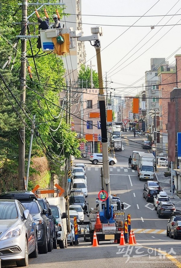 수도권 도시 주택가 왕복 2차선 도로에서 인부 2명이 크레인에 올라 전기 공사를 하고 있다. 차량 유도자(붉은 원)가 차량 유도를 하지 않고 크레인 뒤에 숨어 있다. [사진= 정수남 기자]